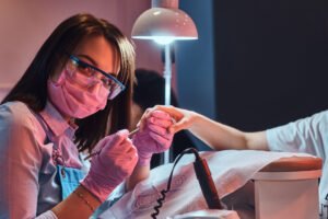 Cheerful manicurist is looking to camera while working on customer’s nails.